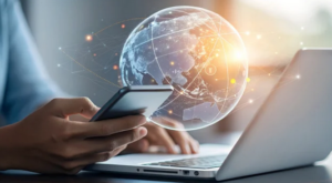 Person, die Smartphone und Laptop bedient, überlagert von einer leuchtenden digitalen Weltkugel mit Netzwerkverbindungen.