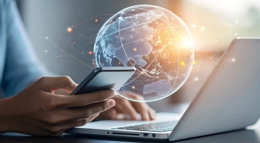 Person, die Smartphone und Laptop bedient, überlagert von einer leuchtenden digitalen Weltkugel mit Netzwerkverbindungen.